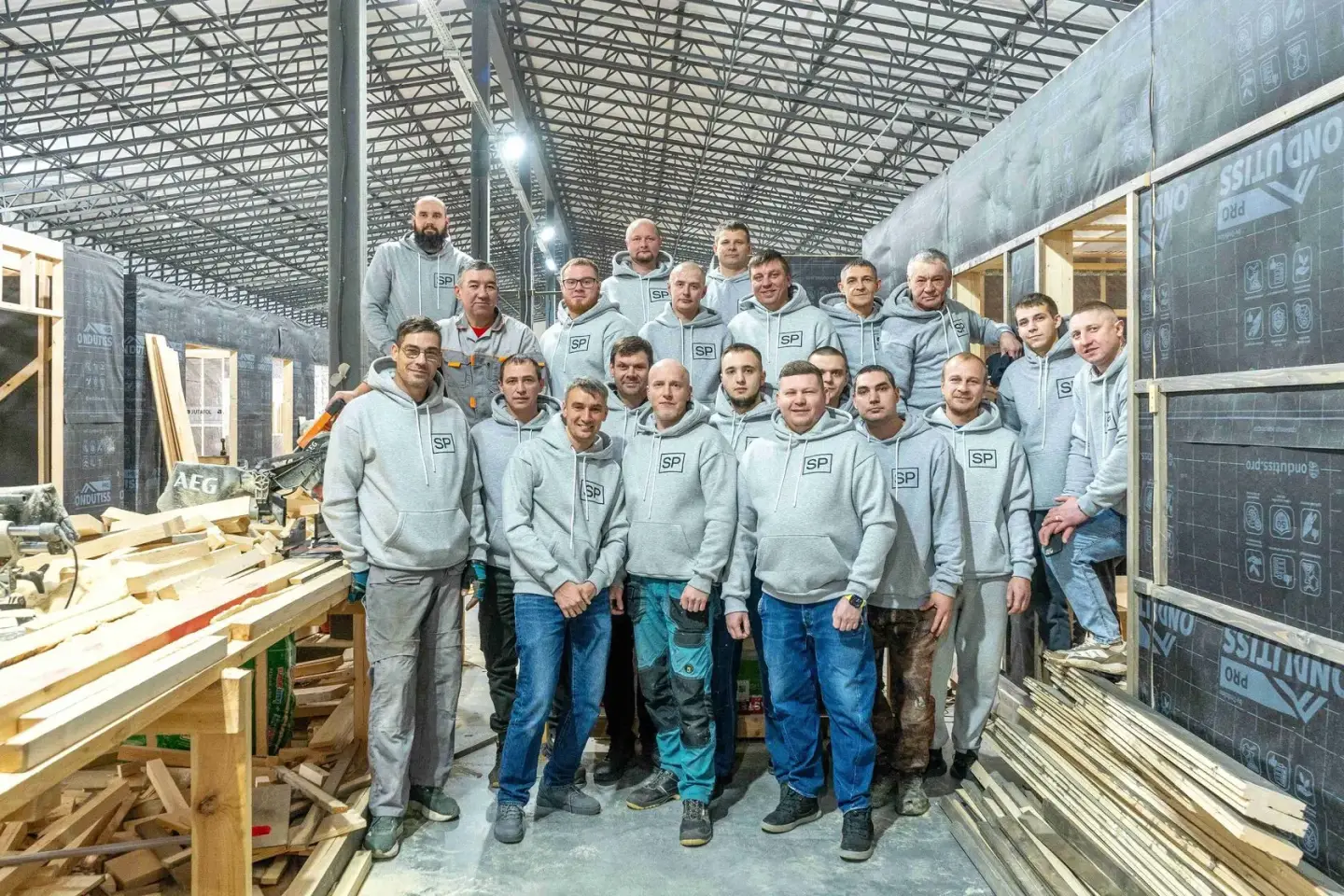 Команда SP Modul в фирменных толстовках в цеху среди строящихся домов